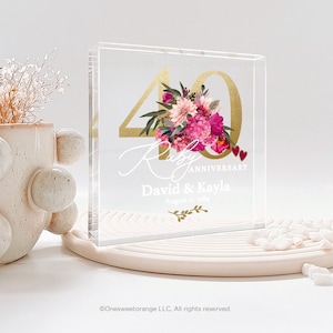 May include: A clear acrylic block with a gold number 40 and pink floral design. The text "Ruby Anniversary" is written in white script with the names "David & Kayla" and the date "August 11, 1984" below.