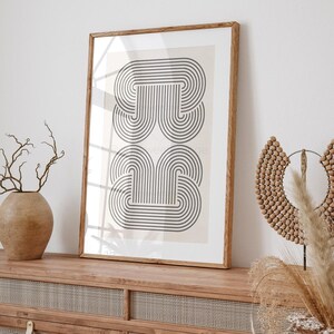 May include: A framed print with a black and white geometric design of overlapping arches. The print is on a cream background and is framed in a natural wood frame.