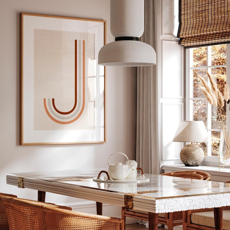May include: A white ceramic pendant light with a black accent hangs over a dining table with a glass top and a white marble base. The table is set with a white teapot and a white cup. A framed print with a geometric design in shades of orange, pink, and gray hangs on the wall behind the table.