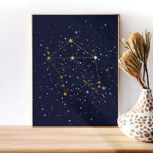 May include: A framed print of the Libra constellation on a dark blue background with gold and blue stars. The constellation is outlined in gold and the word "Libra" is written in gold script.
