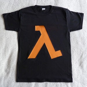 Puede incluir: Camiseta negra con un símbolo Lambda naranja impreso en la parte delantera.