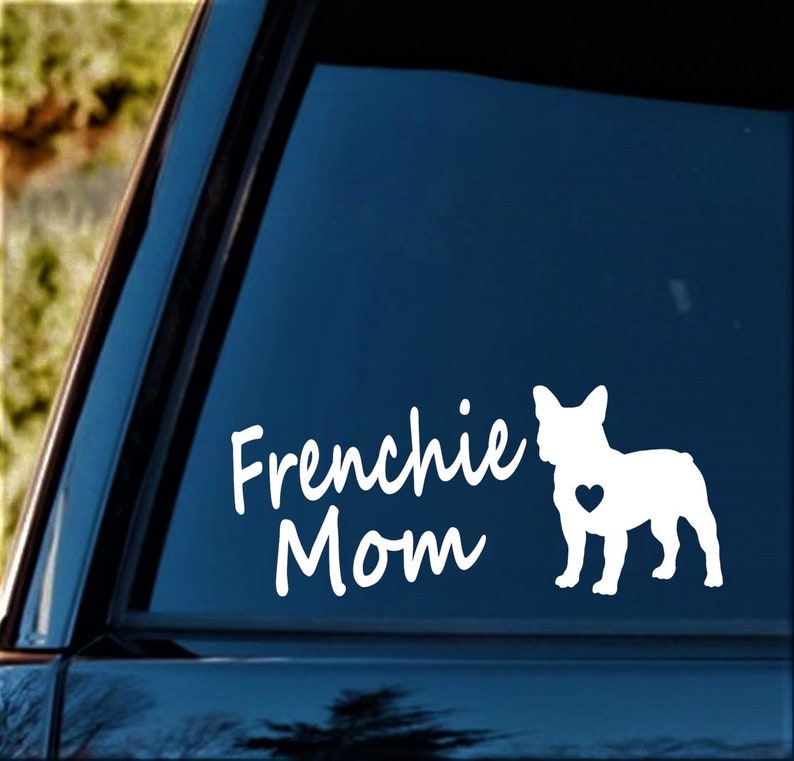 Pu&ograve; includere: Adesivo in vinile bianco con il testo "Frenchie Mom" e una silhouette di un Bulldog Francese con un cuore sul petto. L'adesivo &egrave; su un finestrino di un'auto blu.