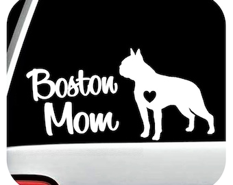 May include: White vinyl decal featuring a silhouette of a Boston Terrier with a heart and the words "Boston Mom" in a script font. The decal is designed for application on a car window or similar surface.