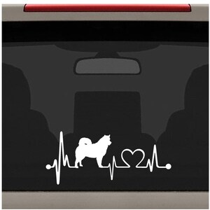 May include: White vinyl decal of a dog silhouette with a heartbeat and a heart. The decal is on a black car window.