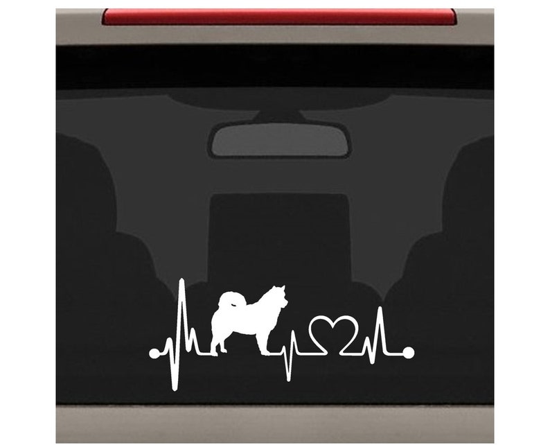 May include: White vinyl decal of a dog silhouette with a heartbeat and a heart. The decal is on a black car window.