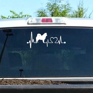 May include: White vinyl decal of a dog silhouette with a heartbeat line and a heart. The decal is on the back window of a truck.