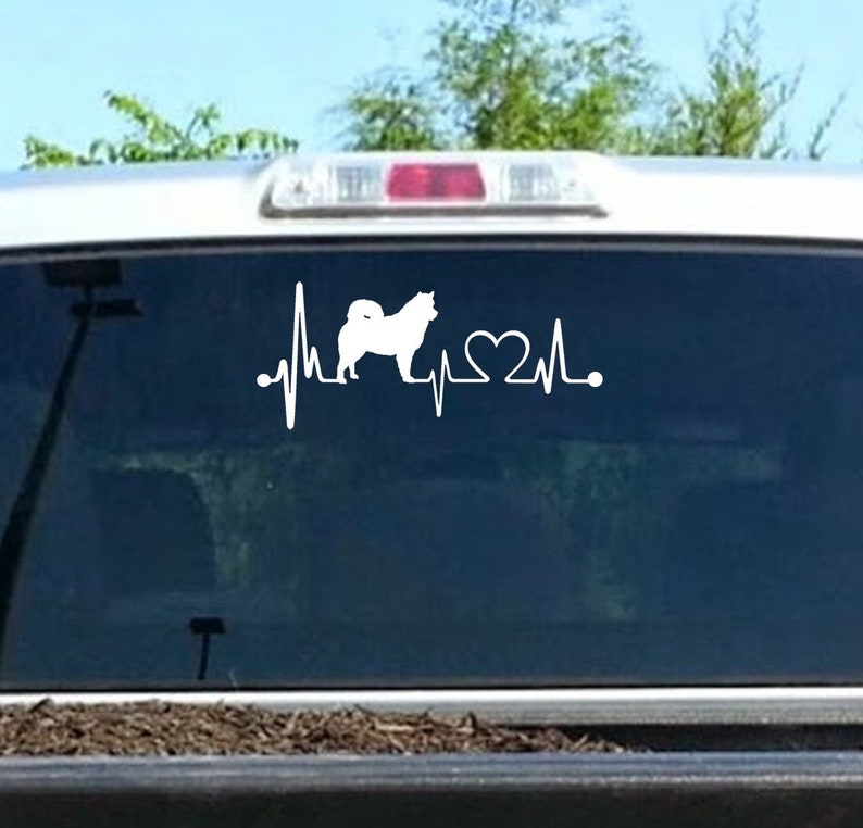 May include: White vinyl decal of a dog silhouette with a heartbeat line and a heart. The decal is on the back window of a truck.