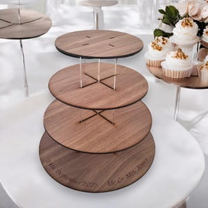 May include: Three-tiered wooden cake stand with a walnut finish. The stand has a clear acrylic rod system to hold the tiers together. The bottom tier is engraved with the text "24th September 2025. Mr & Mrs Jones."