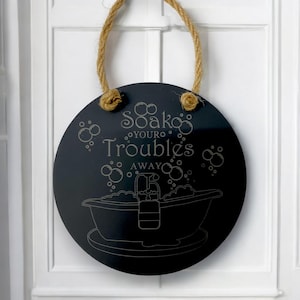 May include: A black round sign with a rope hanger. The sign says "Soak your troubles away" with a bathtub and bubbles illustration.