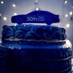 May include: Blue and white cake with a blue car topper that says "Happy Birthday Andrew 50th".
