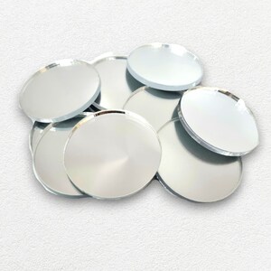 May include: A pile of round, silver-colored, reflective mirror tiles. The tiles are arranged in a random pattern, with some overlapping.