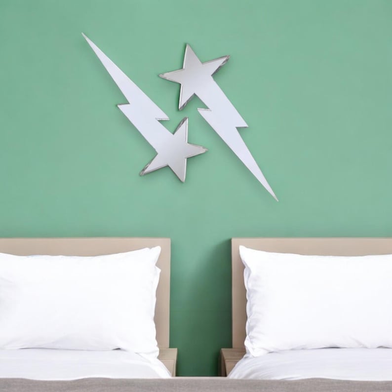 May include: Two silver mirrored lightning bolts with a star shape at the intersection, mounted on a light green wall above two white twin beds with white pillowcases.