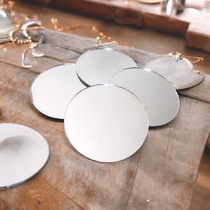 May include: Five round, silver-rimmed mirrors of varying sizes are arranged in a cluster on a wooden surface. The mirrors are all reflective and show a blurred image of the surrounding area.
