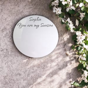 May include: A round, white mirror with a black border. The mirror has the text "Sophie You are my Sunshine" written on it.