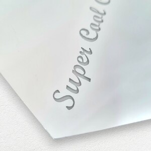 May include: Close-up of a white surface with the text "Super Cool" written in a cursive font.