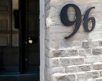 May include: Black metal house number 96 on a white brick wall.
