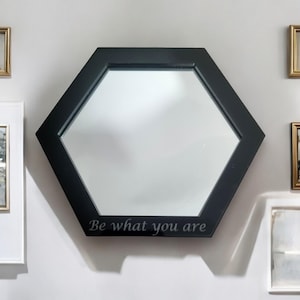 May include: A black hexagonal mirror with a beveled edge and the text "Be what you are" inscribed on the bottom.
