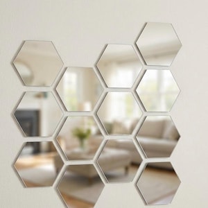 May include: A set of hexagonal mirrors mounted on a white wall. The mirrors reflect a room with a fireplace, sofa, and windows, offering a contemporary and decorative wall feature.