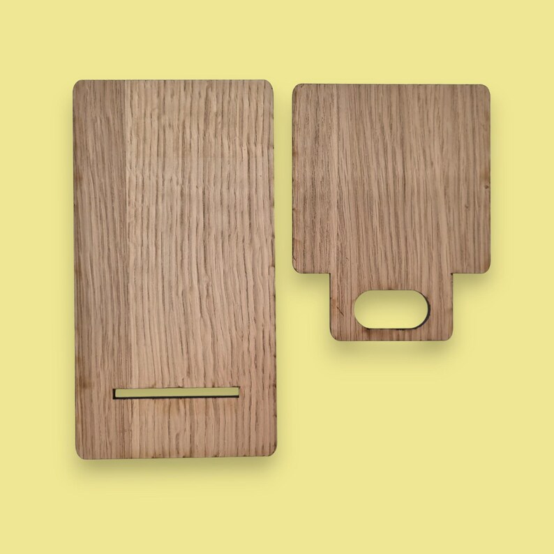 May include: Two wooden cutting boards with a light brown color and visible wood grain. One board is rectangular with a slot, and the other is square with a handle cutout. The boards are on a yellow background.