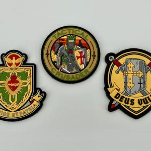 May include: Three embroidered patches with military and religious themes. One patch features a crusader with a rifle, another has a shield with a heart and dove, and the third displays a shield with crossed swords and the text "Deus Vult".