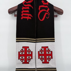 Könnte beinhalten: Schwarz-weißer Strickschal mit roter Schrift und Kreuzmotiven. Das Wort "Jerusalem" steht in roter Schrift oben. Der untere Teil zeigt zwei rote Jerusalemer Kreuze auf weißem Grund, mit schwarzen und goldenen Streifen und einem Fransenrand.