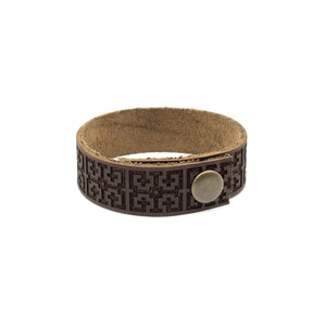 May include: A brown leather bracelet with a geometric pattern and a brass button closure.