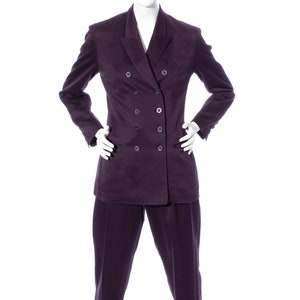 Pu&ograve; includere: Un abito doppiopetto di colore viola scuro. Il completo comprende una giacca con revers a punta e un paio di pantaloni abbinati.