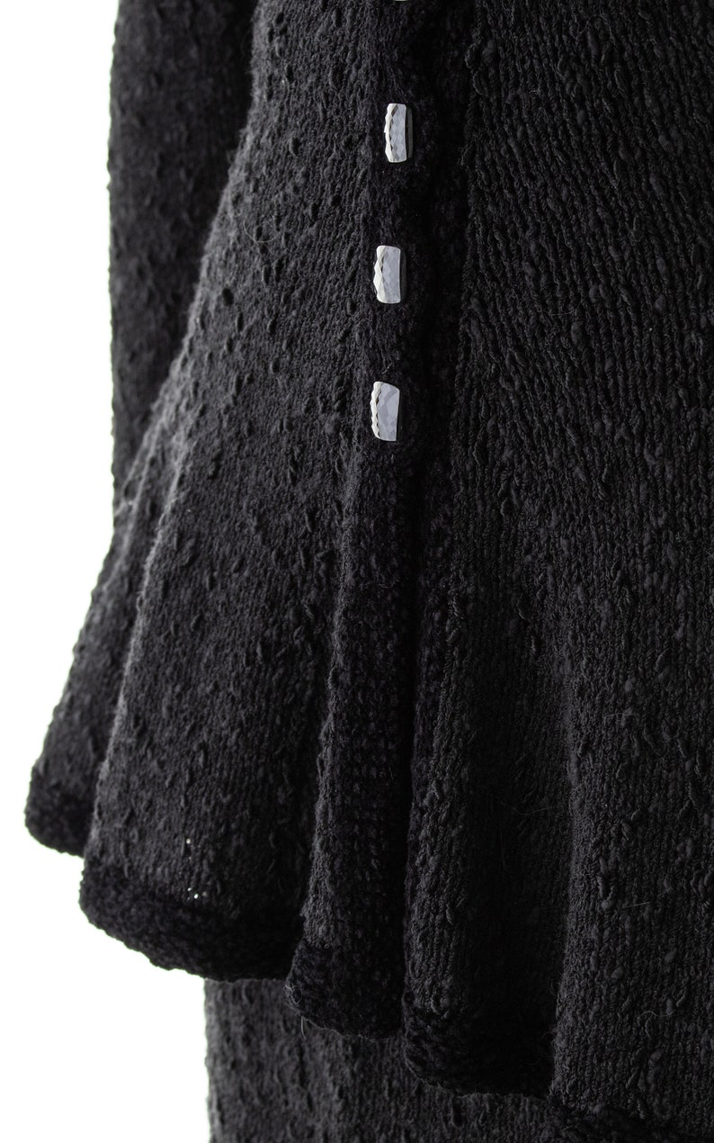 May include: Black knitted dress with a ruffled hem and white buttons down the front.