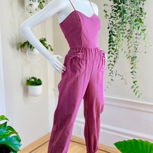 May include: A pink and white striped jumpsuit with a sweetheart neckline and cuffed legs. The jumpsuit has pockets on the front and is made of a lightweight fabric.