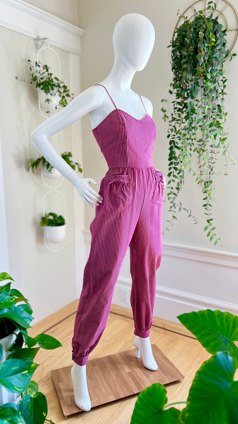 May include: A pink and white striped jumpsuit with a sweetheart neckline and cuffed legs. The jumpsuit has pockets on the front and is made of a lightweight fabric.