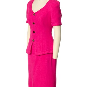 May include: A pink short-sleeved dress suit with a skirt and a fitted jacket. The jacket has a V-neckline and a button-up front.