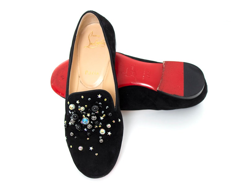 May include: Black suede loafers with a red sole and a cluster of colorful jewels and stars on the toe.