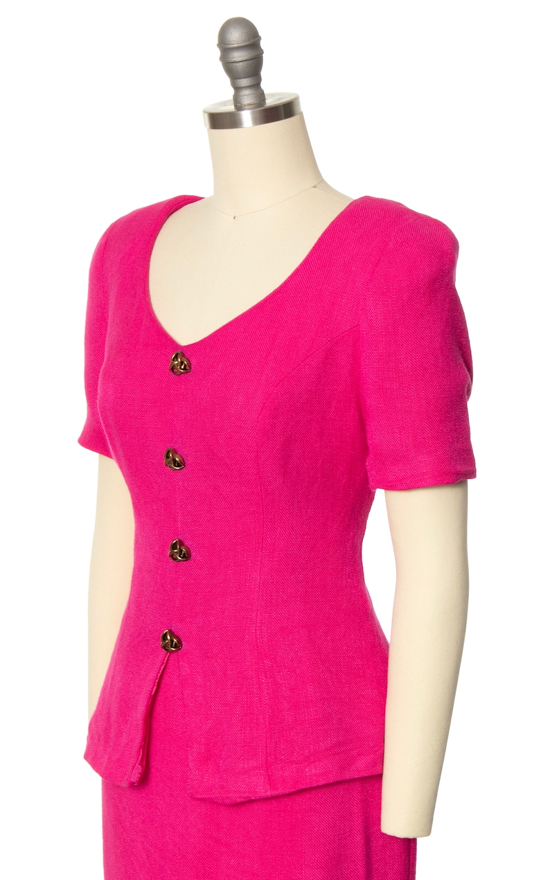 May include: A hot pink short-sleeved dress with a v-neck and button closure. The dress has a fitted bodice and a skirt that falls to the knees.
