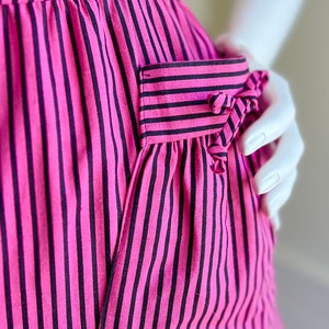 May include: A pink and black striped dress with a patch pocket on the side. The pocket has a bow detail.