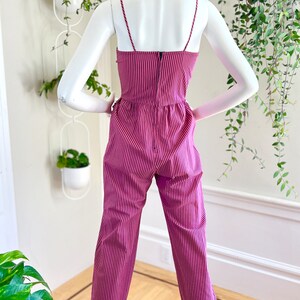 May include: A pink and black striped jumpsuit with thin straps and a fitted bodice. The jumpsuit has a relaxed fit through the legs and features a cuffed hem.