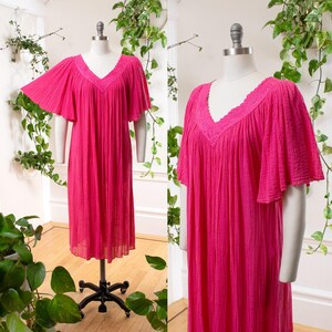 May include: A bright pink, knee-length dress with a V-neckline and short, flutter sleeves. The dress features a textured fabric and a delicate lace trim around the neckline. The dress is displayed on a mannequin.