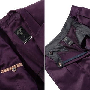 Pu&ograve; includere: Una giacca di completo e pantaloni abbinati di colore viola con un dettaglio di tasca marrone. La giacca ha un'etichetta che recita "Jean Paul Gaultier Homme" e "34".