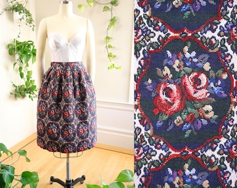 May include: A vintage knee-length skirt with a floral pattern. The skirt features a dark background with repeating oval designs containing red roses and other flowers. The skirt is displayed on a mannequin with a white bustier.