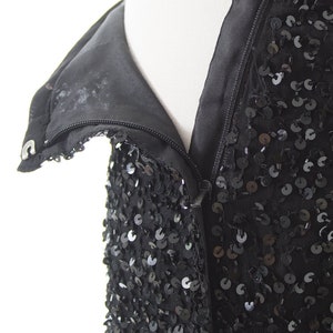 Puede incluir: Un vestido negro de lentejuelas con cierre de cremallera. El vestido est&aacute; hecho de una tela suave y fluida y est&aacute; adornado con lentejuelas.