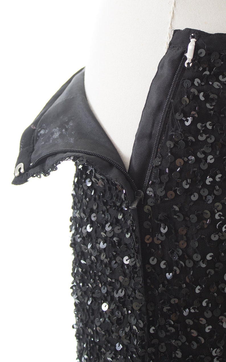 Puede incluir: Un vestido negro de lentejuelas con cierre de cremallera. El vestido est&aacute; hecho de una tela suave y fluida y est&aacute; adornado con lentejuelas.
