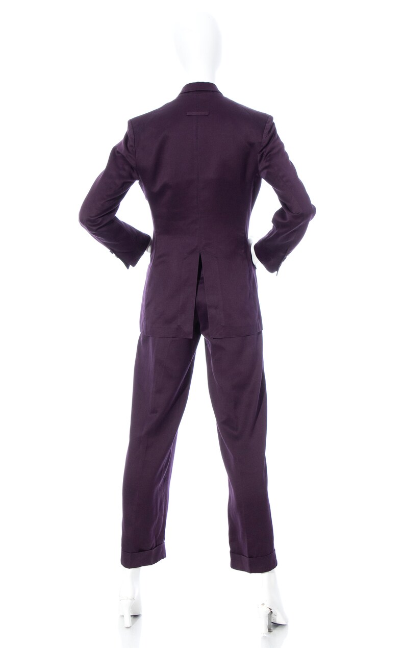 Pu&ograve; includere: Un completo viola con giacca e pantaloni. Il completo &egrave; su un manichino bianco.