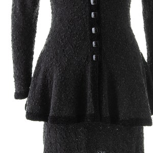 May include: Black knitted dress with a fitted bodice and a flared skirt. The dress has a V-neckline and a row of black buttons down the front.