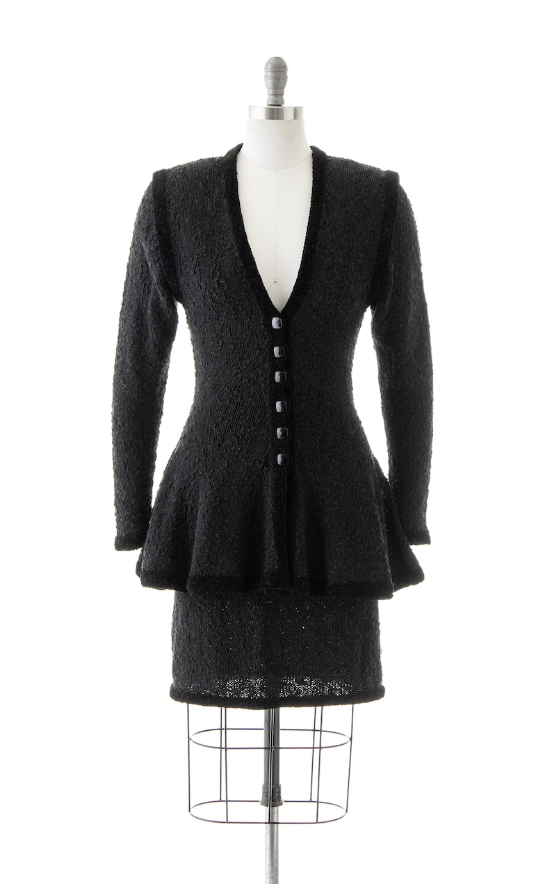 May include: A black knit sweater dress with a ruffled skirt and a button-up front.