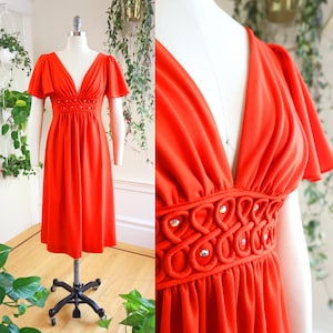 May include: A bright orange maxi dress with a deep V-neckline and short, flared sleeves. The dress has a beaded detail at the waist and a flowing skirt.