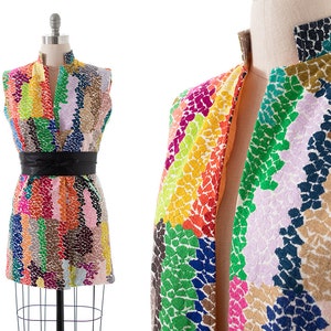 May include: A sleeveless dress with a colorful abstract pattern. The dress has a black belt and a high neckline.