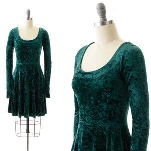 May include: A green velvet dress with long sleeves and a scoop neckline. The dress has a fitted bodice and a flared skirt.