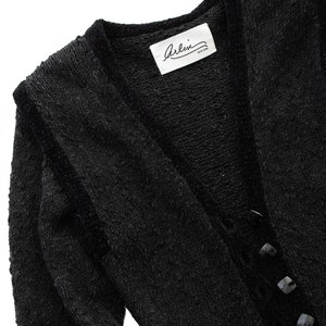 May include: Black long-sleeved cardigan with a V-neck and button closure. The cardigan has a textured knit and a label that reads "Arlini New York".