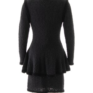 May include: Black knit dress with a ruffled skirt and a fitted bodice. The dress is on a mannequin.