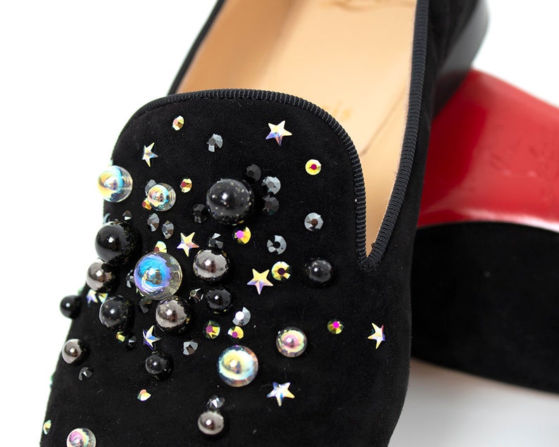 May include: Black suede loafers with a star and jewel embellishment. The loafers have a pointed toe and a low heel.