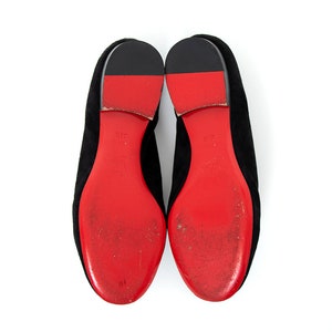 May include: A pair of black suede flats with red leather soles. The soles have a distinctive red color and a slightly worn appearance.
